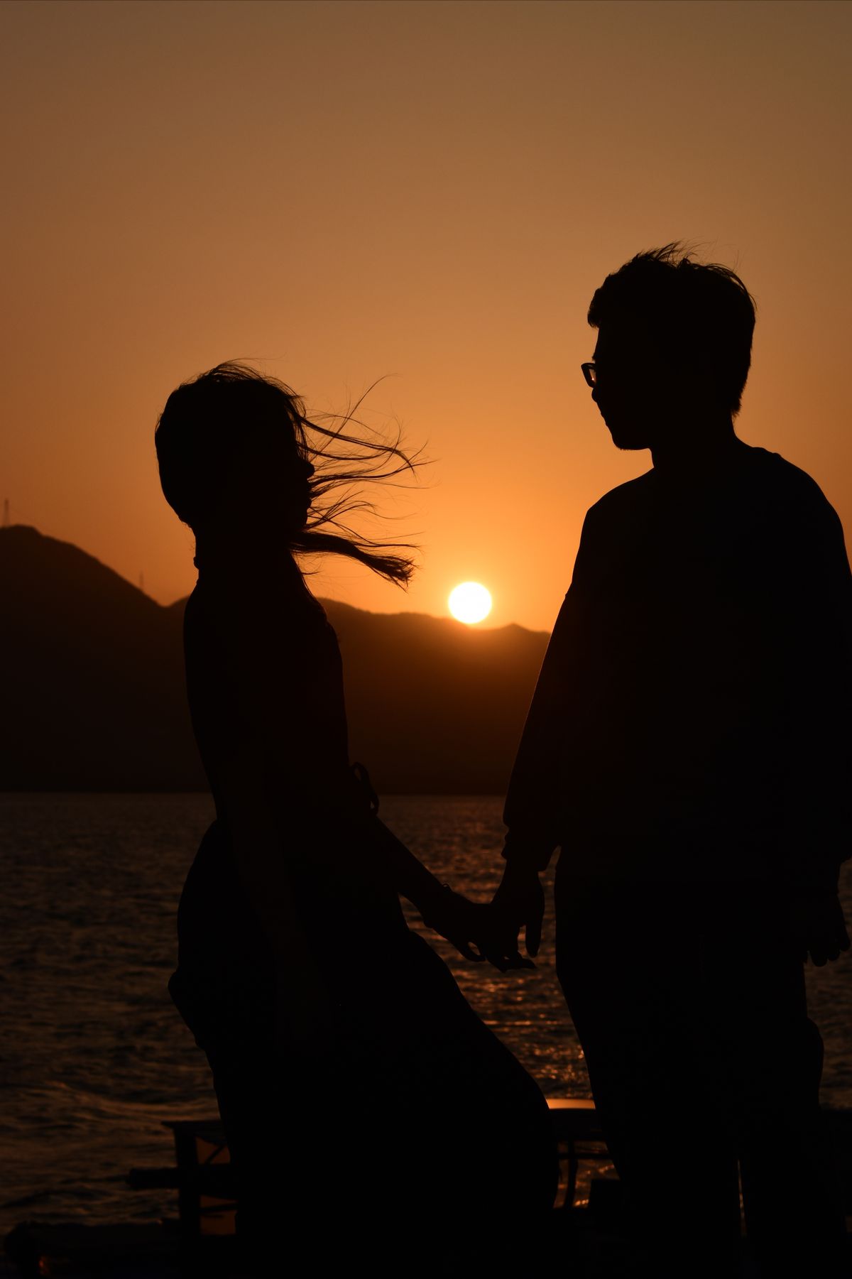 A couple silhouetted against the sun setting over the sea